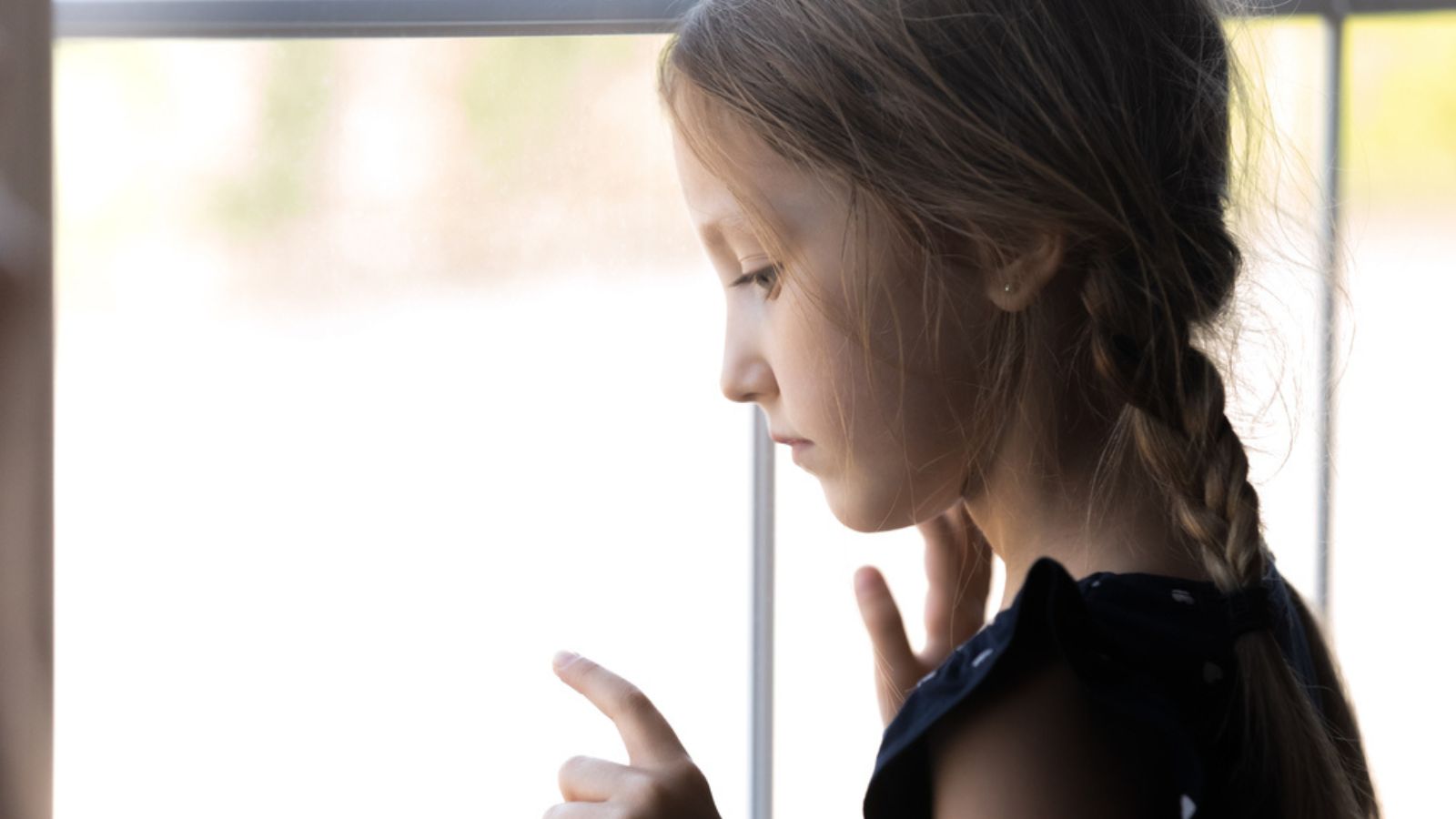 Sad little girl looking out window