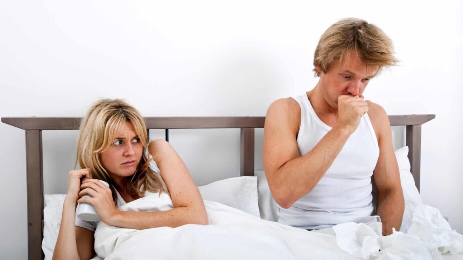 Scared woman looking at man coughing in bed