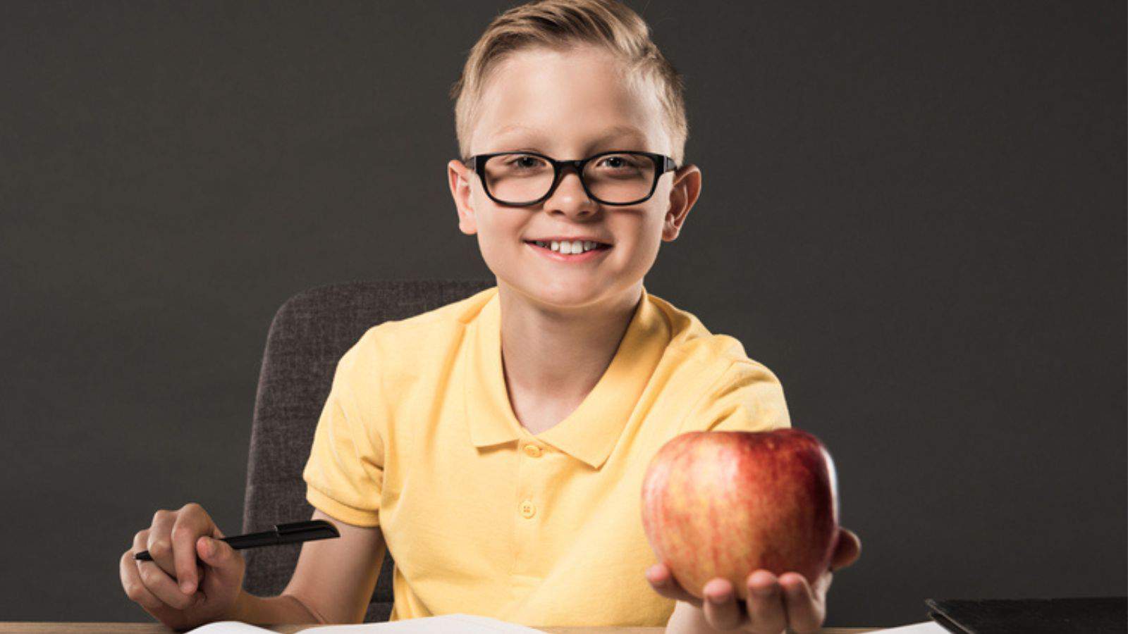 Schoolboy in eyeglasses holding apple and doing homework