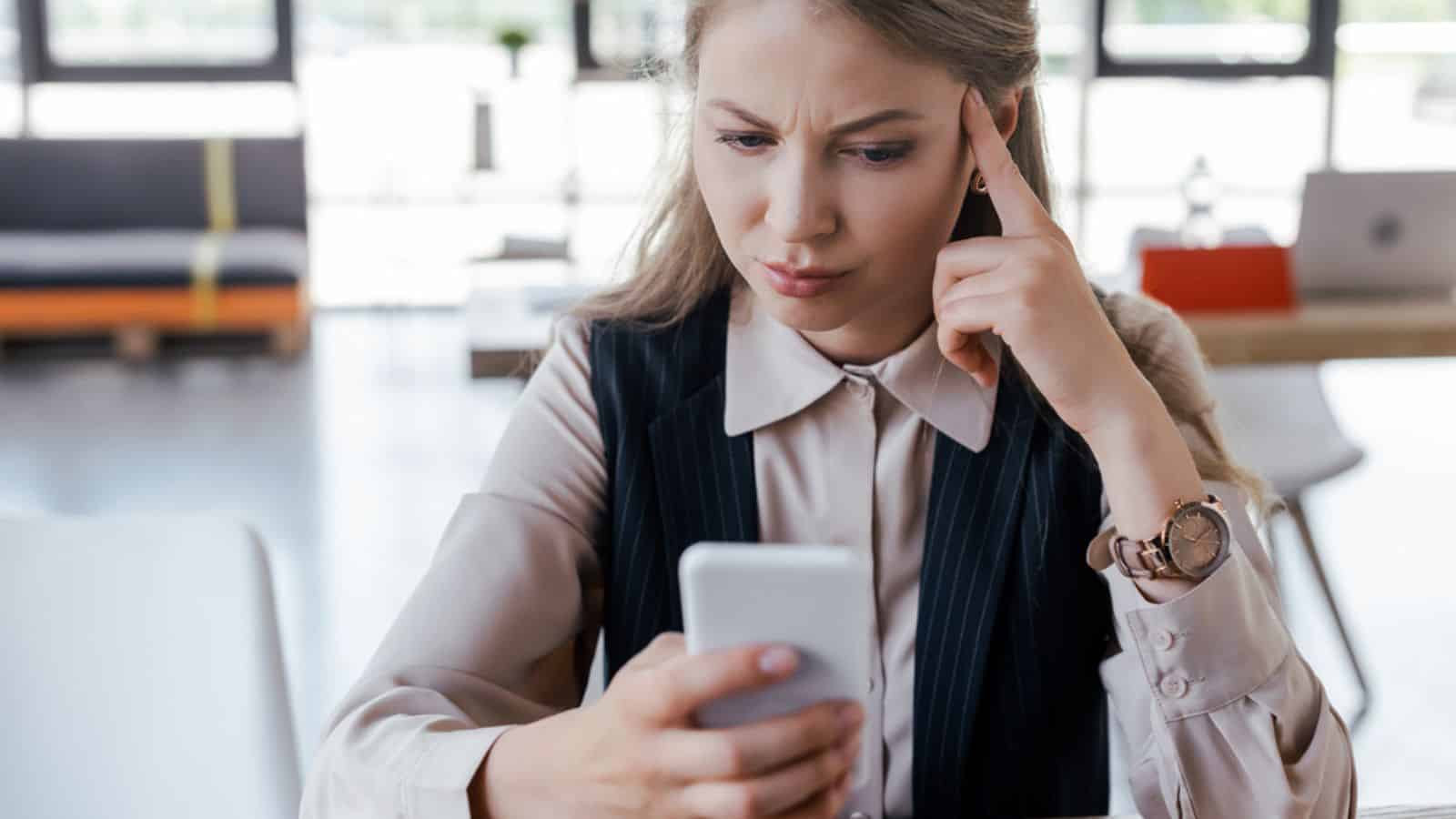 Selective focus of dissatisfied businesswoman using smartphone in office