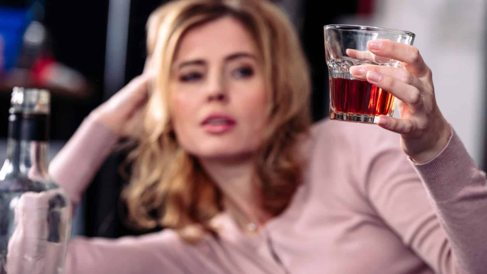 Selective focus of woman looking at glass of alcohol in hand
