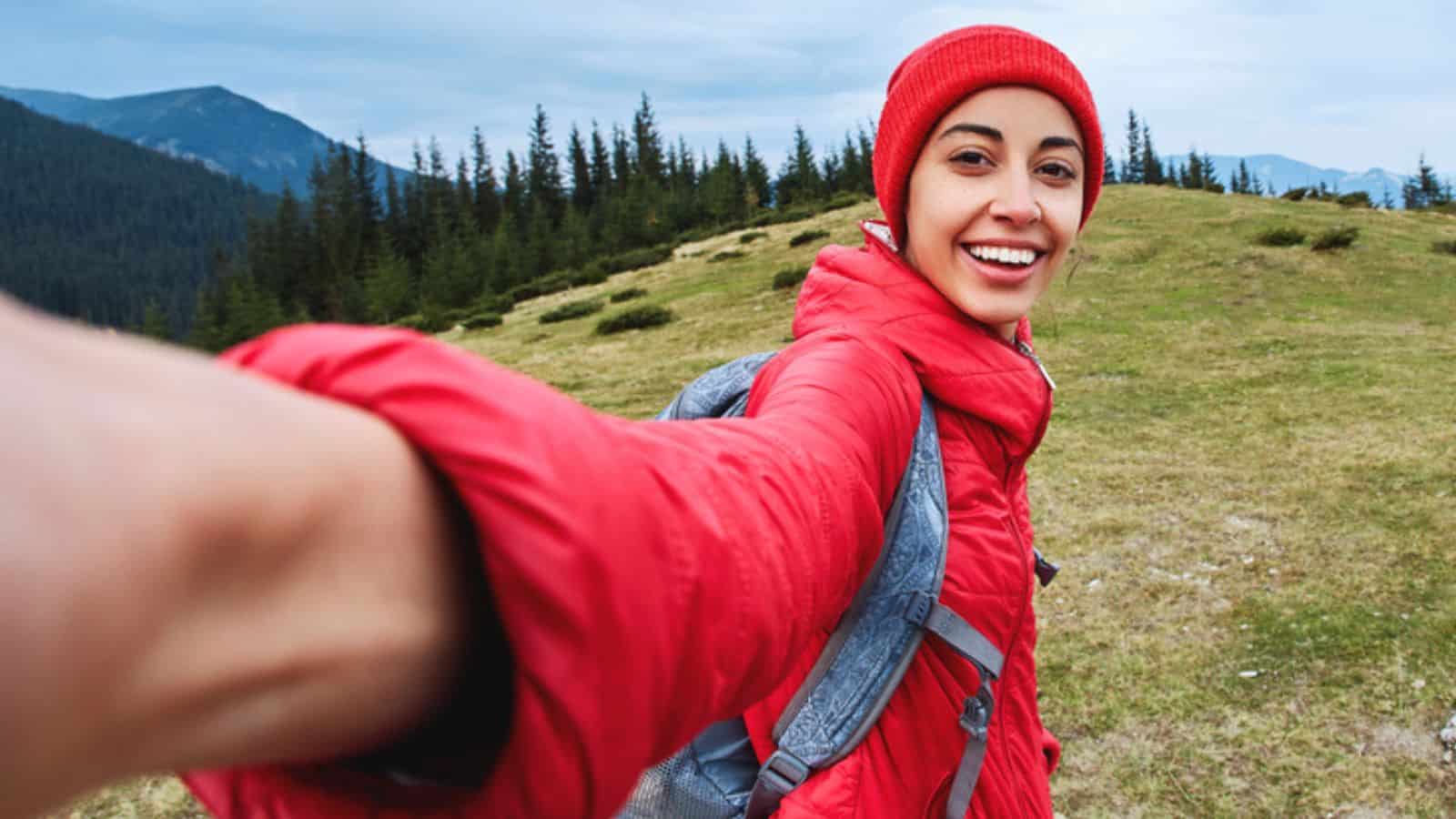 Selfie image of a young smiling woman hiker with small backpack