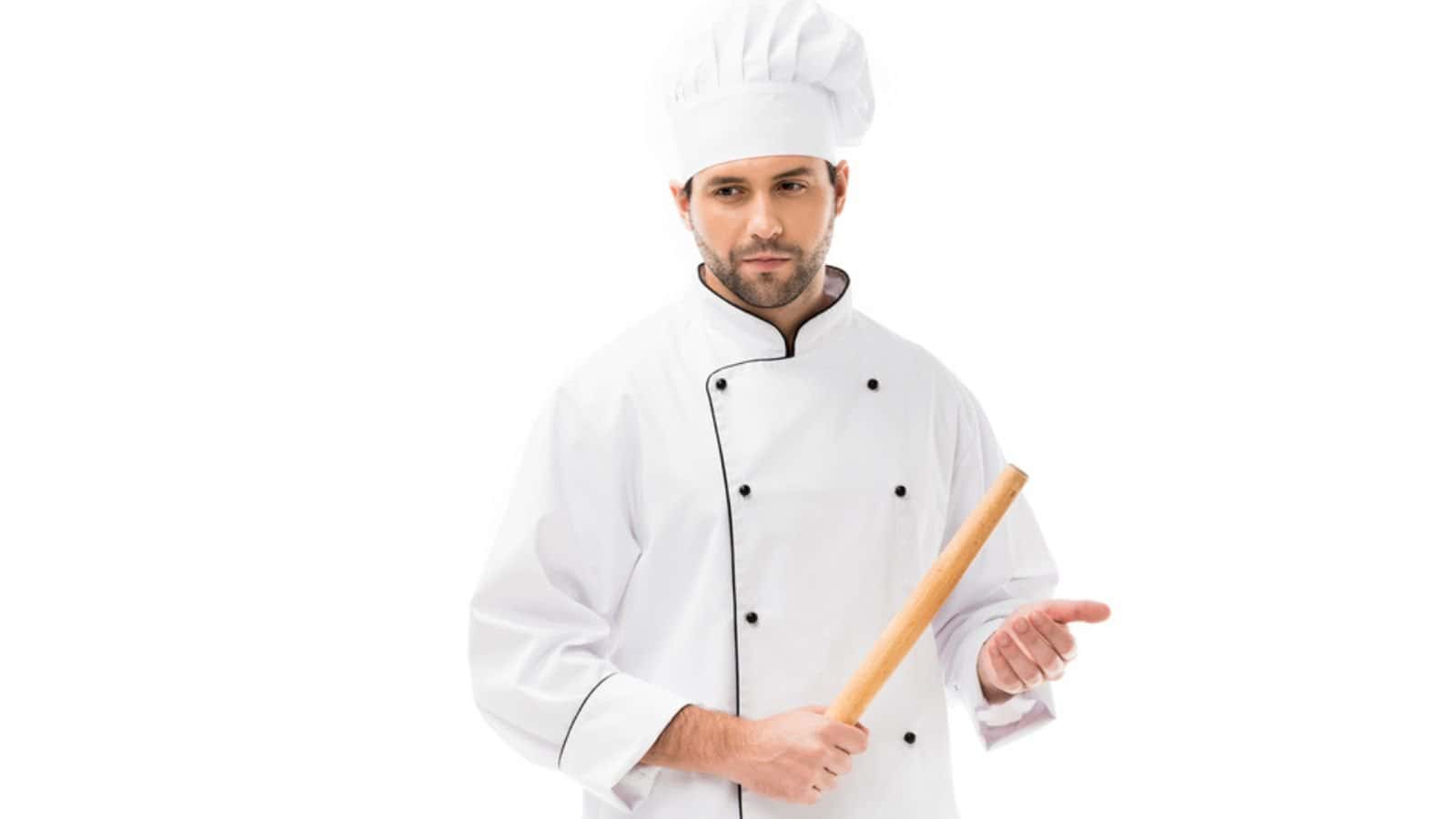 Serious young chef holding rolling pin isolated on white