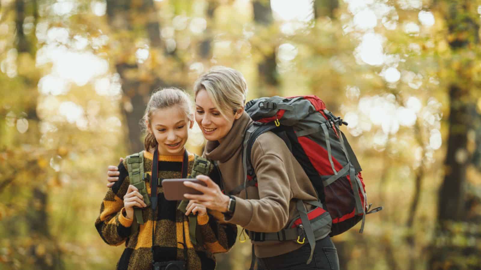 Shot of a teen girl and her mom using smart phone during walk together through the forest in autumn