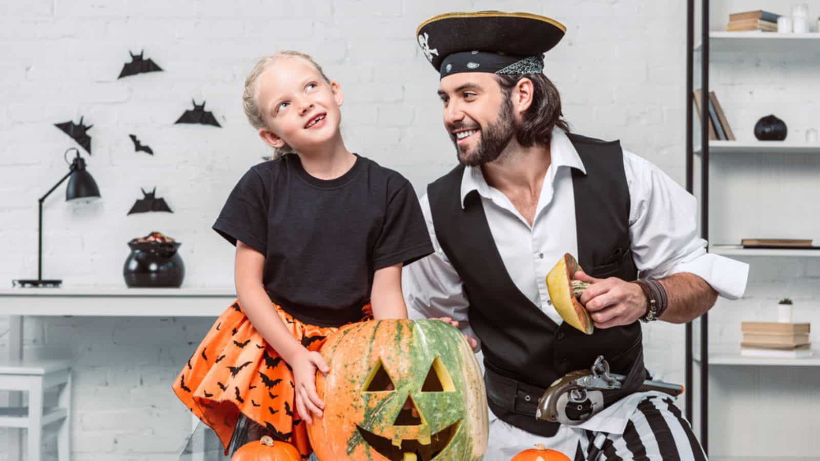 Smiling father and daughter in halloween costumes at table