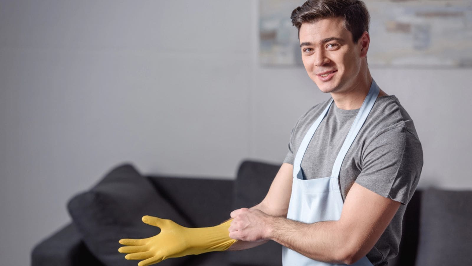 Smiling handsome man wearing rubber glove for cleaning in living room