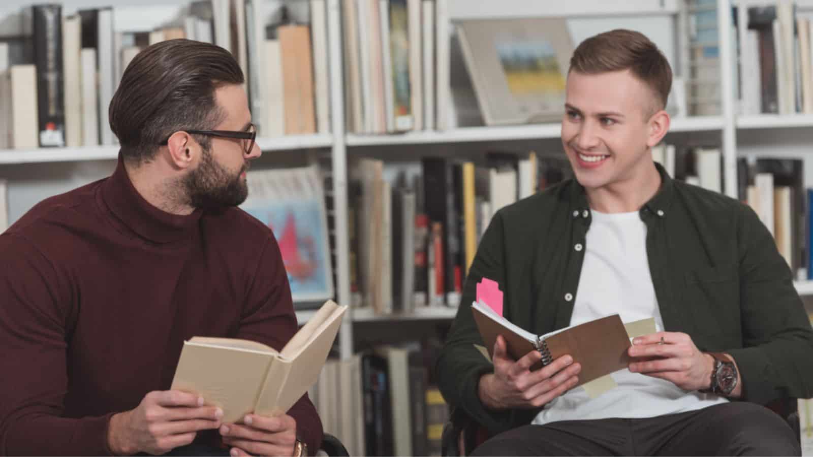 Smiling handsome men sitting with books in library