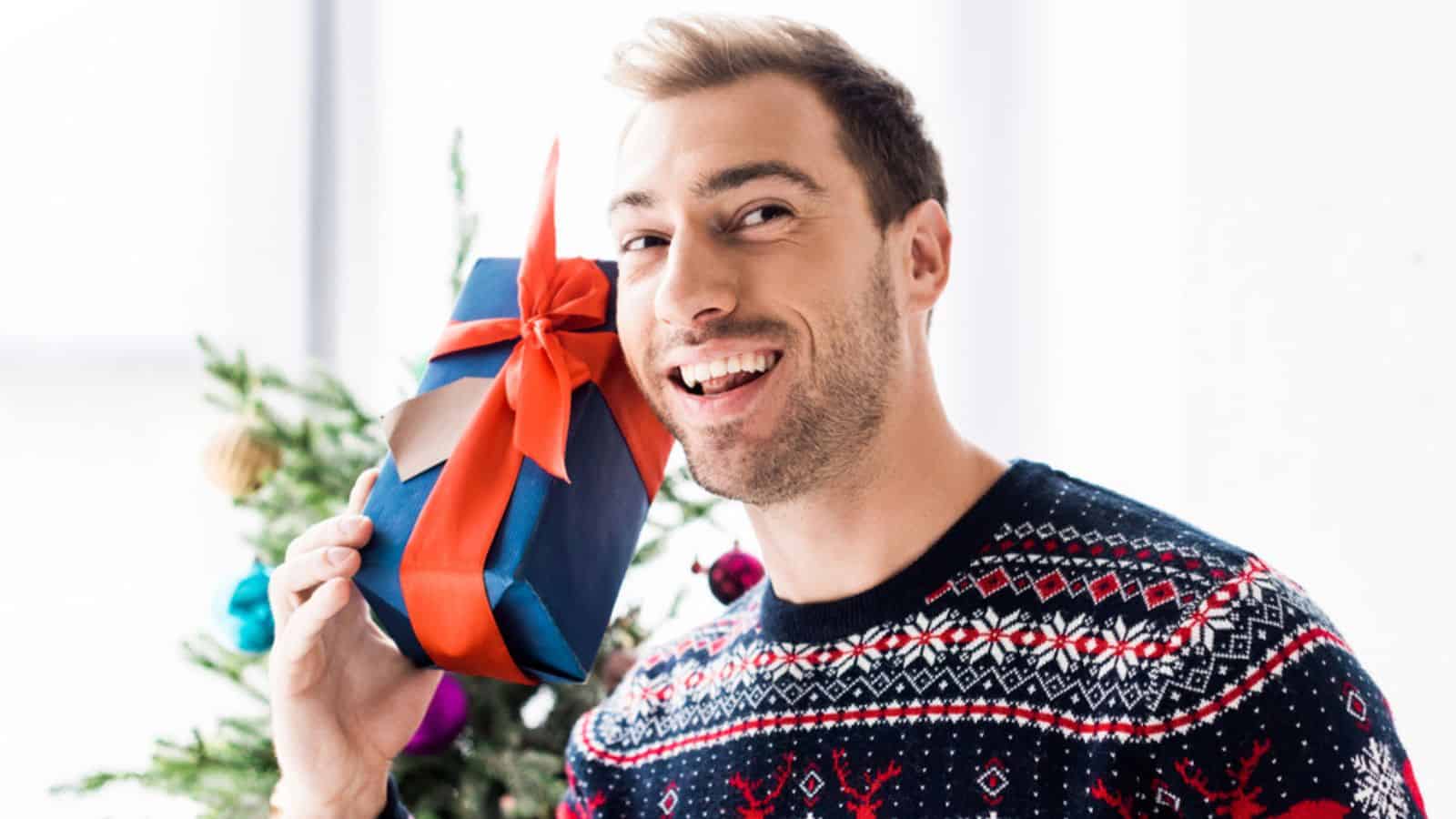 Smiling man in christmas sweater with gift box near head