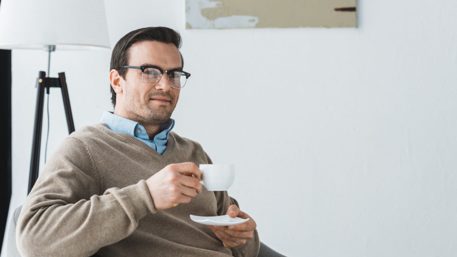 Smiling man in glasses sitting in chair and drinking coffee
