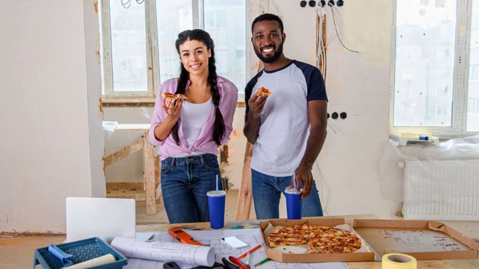 Smiling young couple eating pizza while making renovation of home
