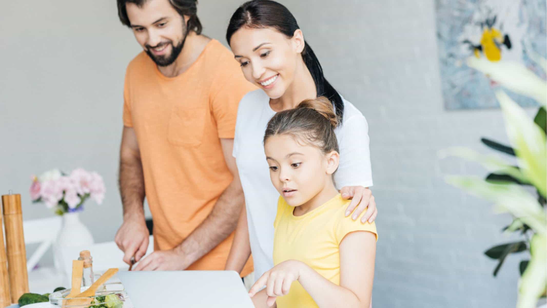 Smiling young family using laptop together at kitchen