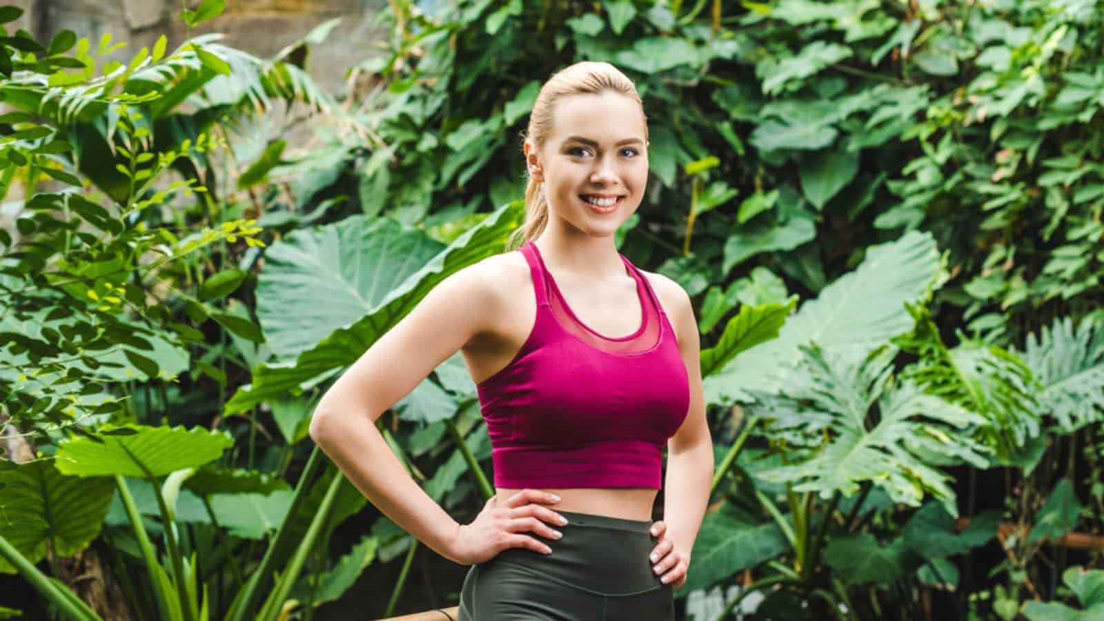Smiling young woman in modern sportswear looking at camera in park