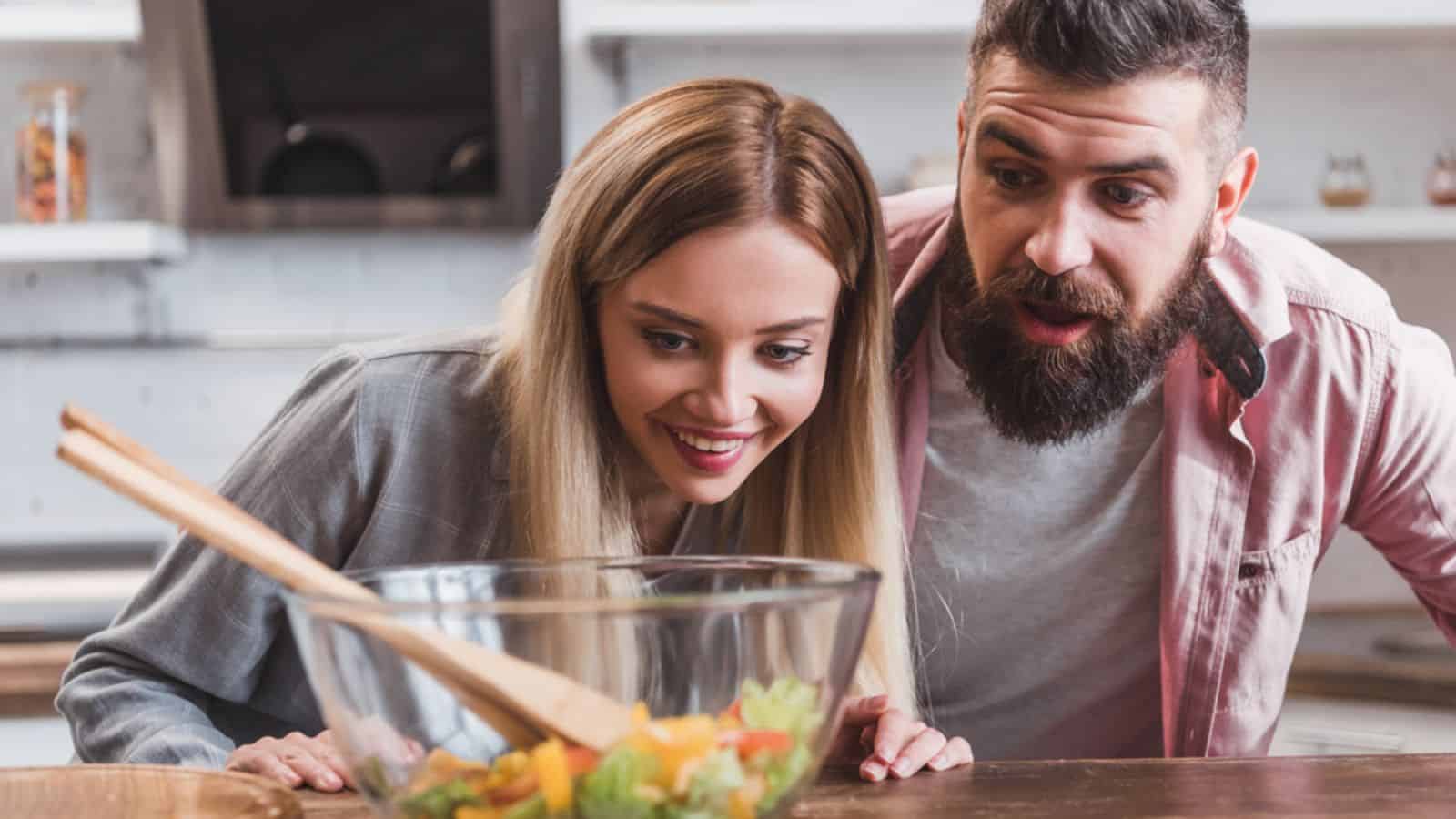 Surprised cheerful couple looking at salad in glass bowl