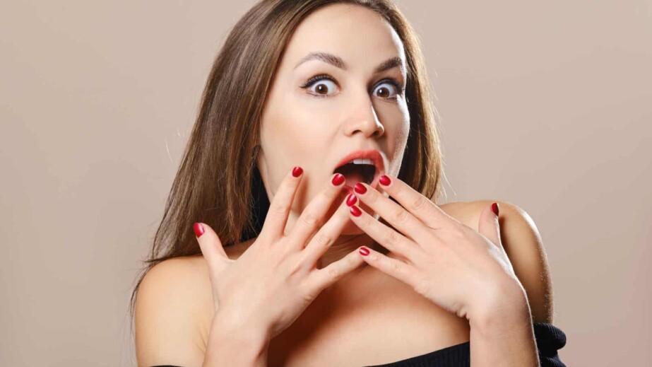Surprised woman covers open mouth with fingers