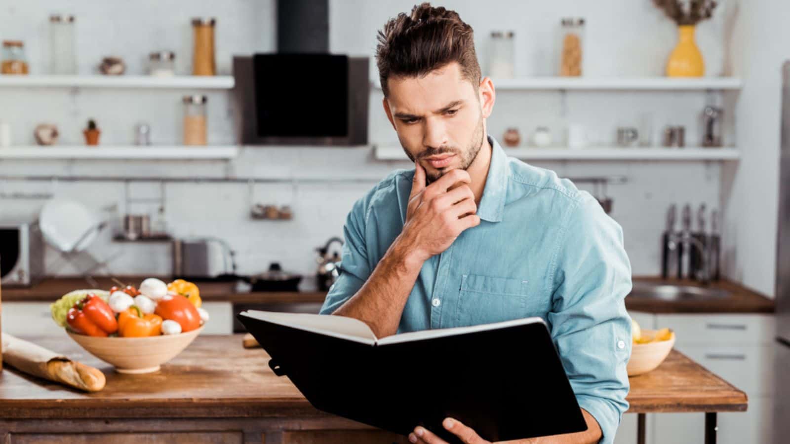 Thoughtful handsome young man reading cookbook