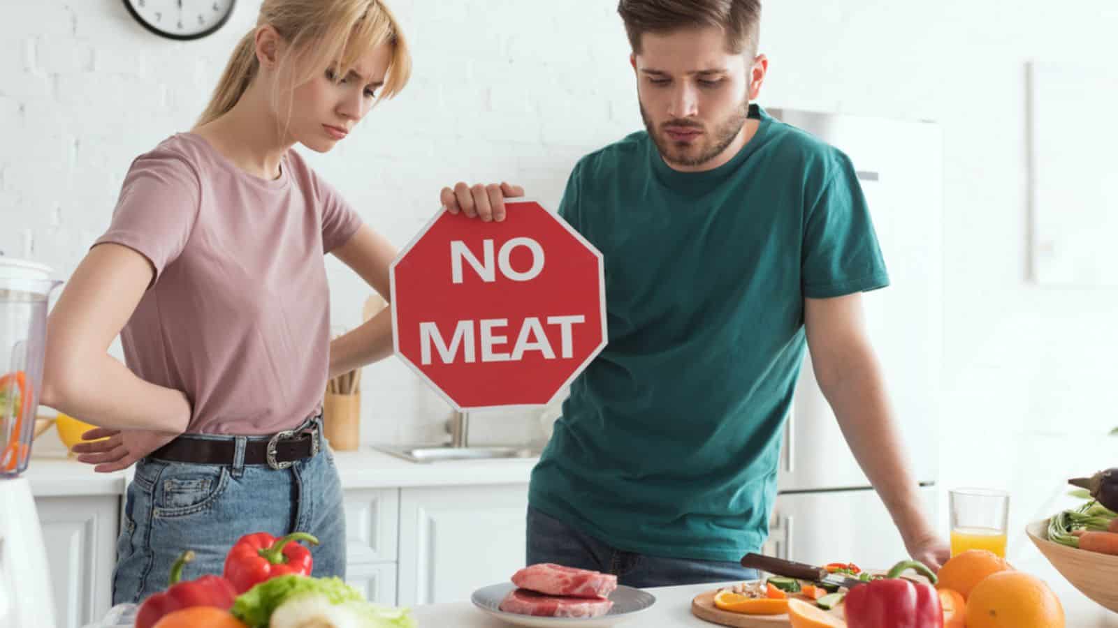 Vegan couple with no meat sign at table with raw meat 
