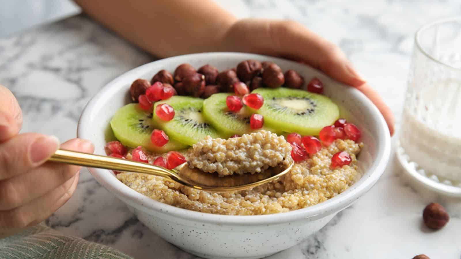 Woman eating quinoa porridge with hazelnuts, kiwi and pomegranate seeds at marble table