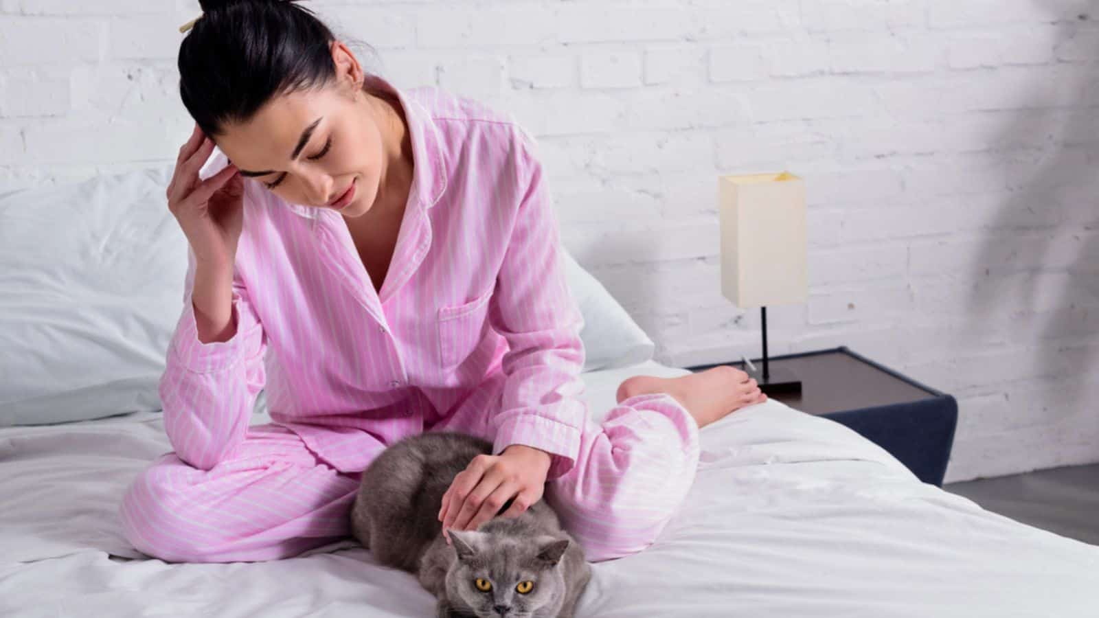 Woman in pajamas with britain shorthair cat resting on bed at home