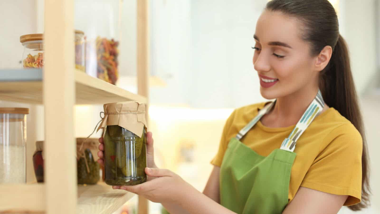 Woman putting jar of pickles on shelf indoors