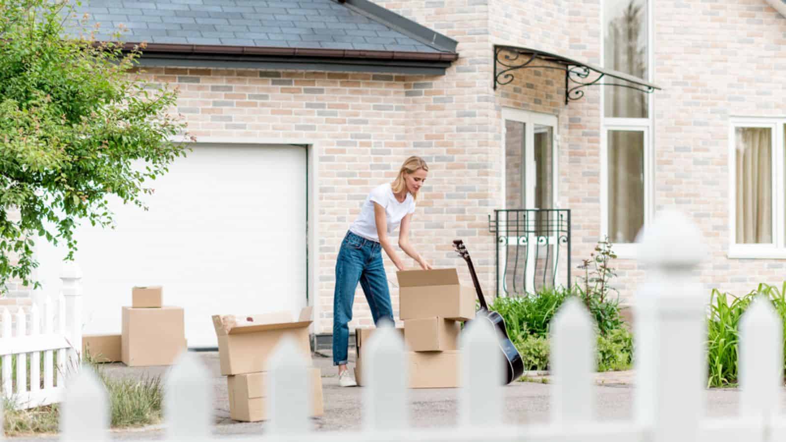 Woman unpacking cardboard boxes near guitar in front of new house