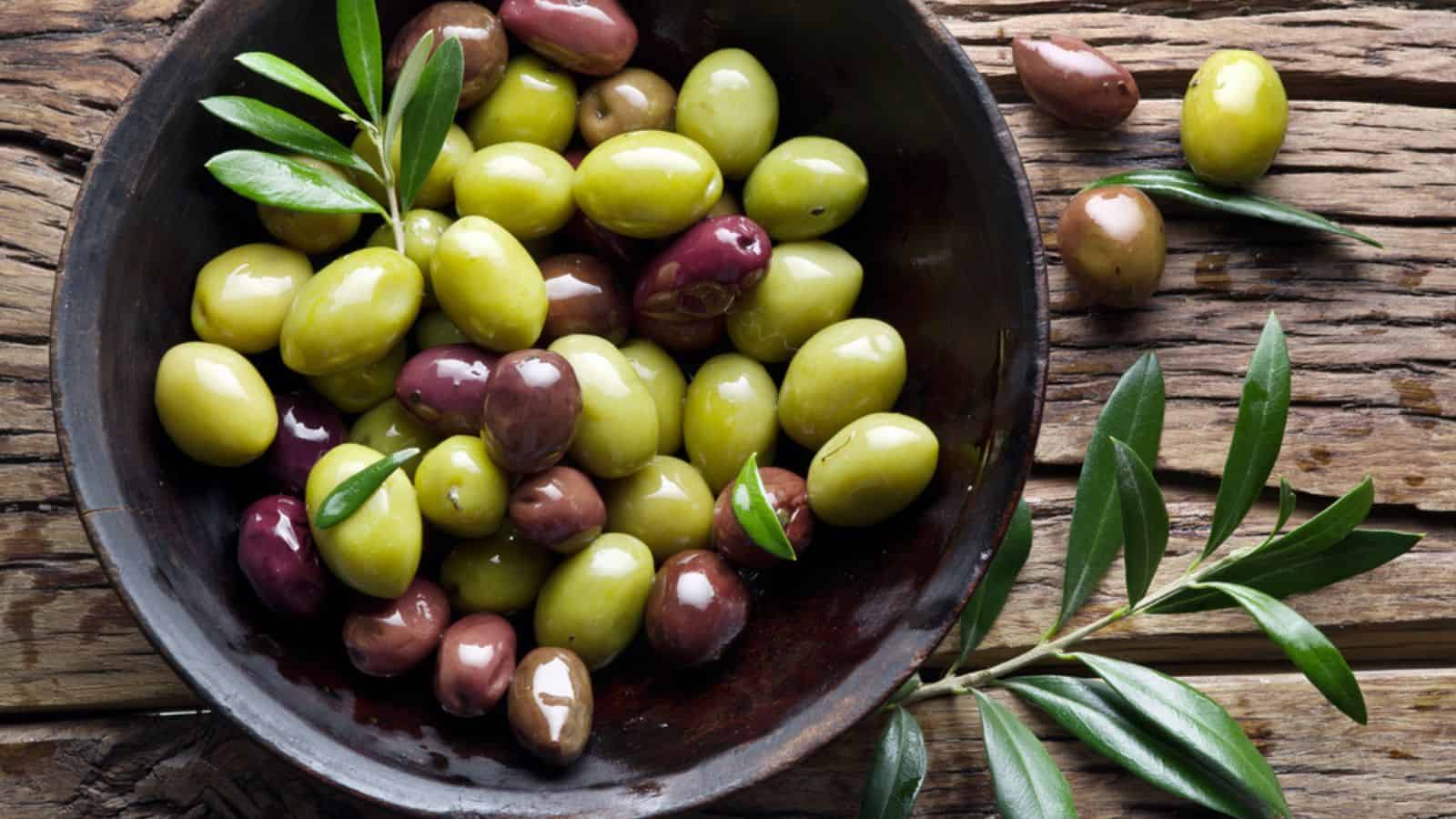 Wooden bowl full of olives and olive twigs besides it