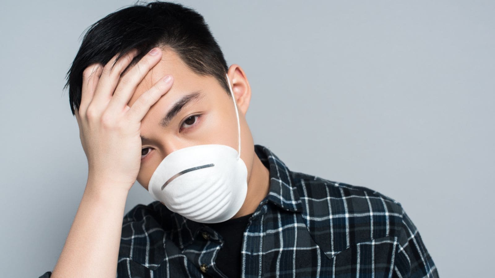 Young asian man in respirator mask touching forehead