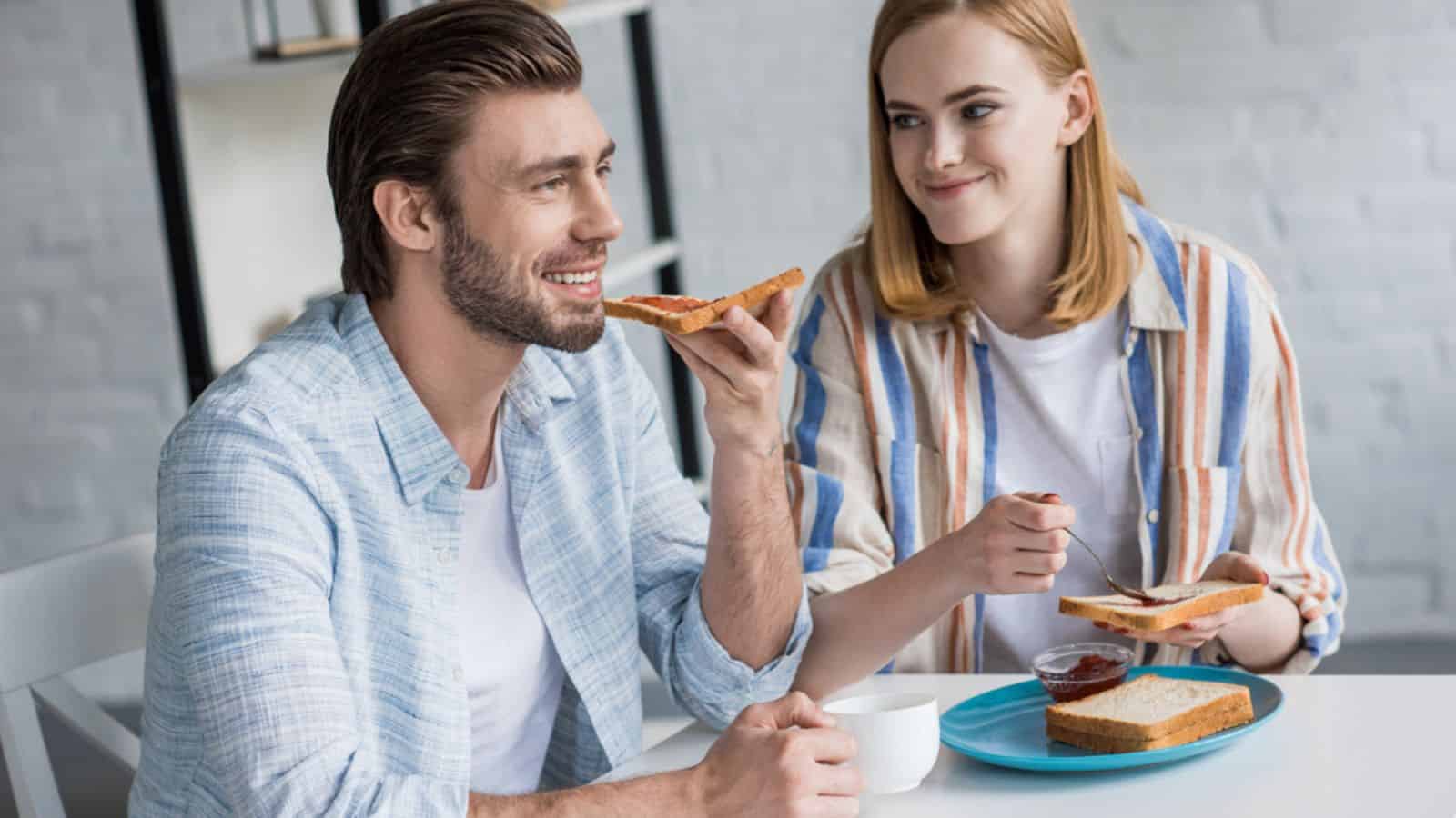 Young couple eating toasts with jam during breakfast at table