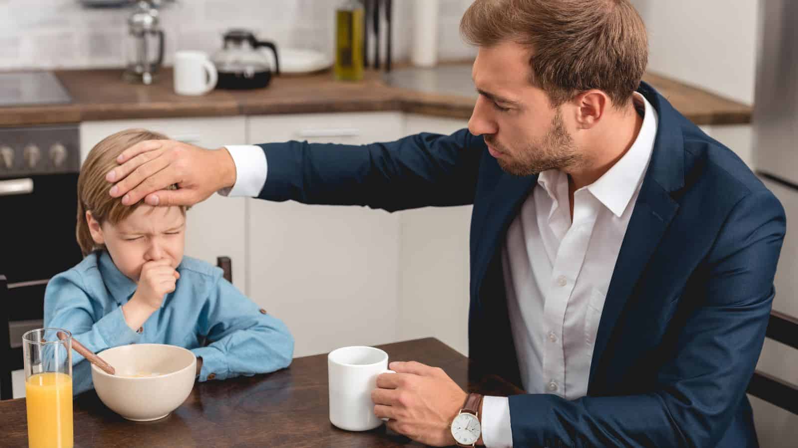 Young father checking temperature of son with hand during breakfast