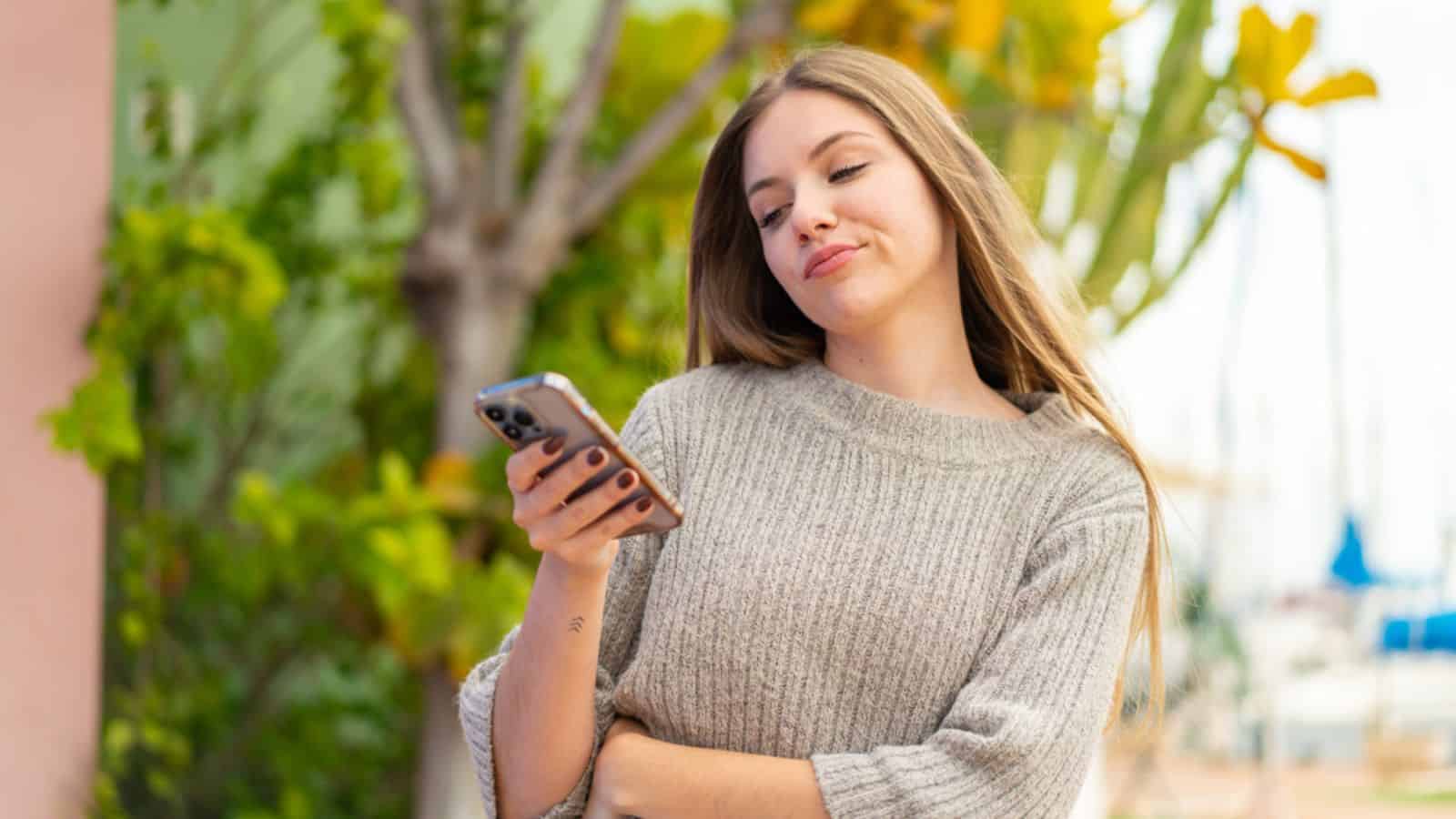 Young pretty blonde woman using mobile phone at outdoors with sad expression