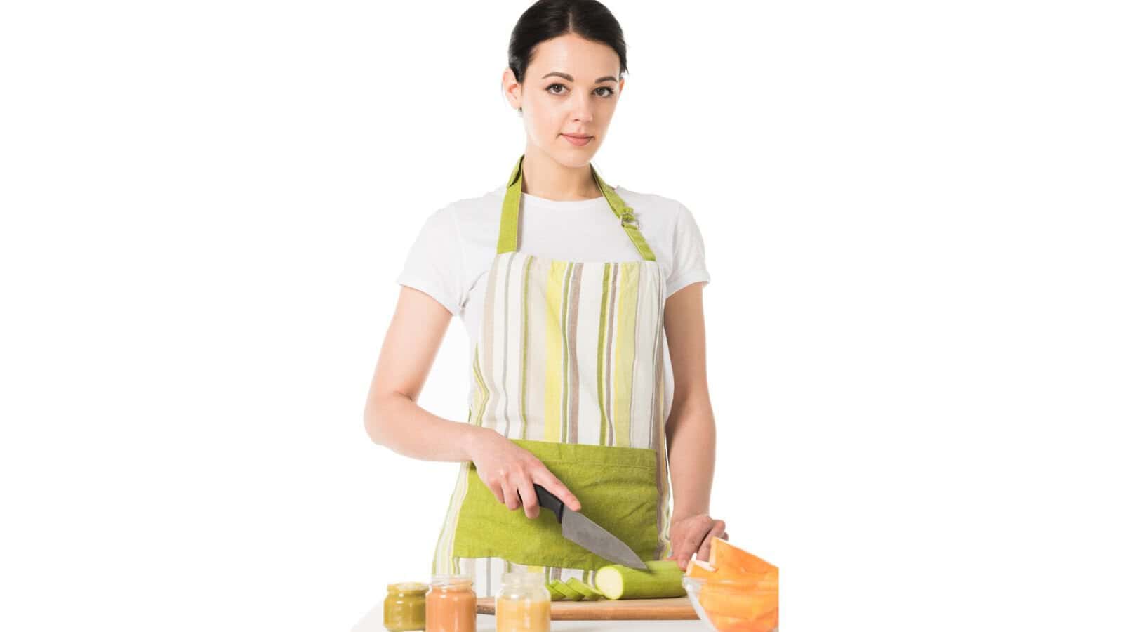 Young woman in apron cutting zucchini by knife