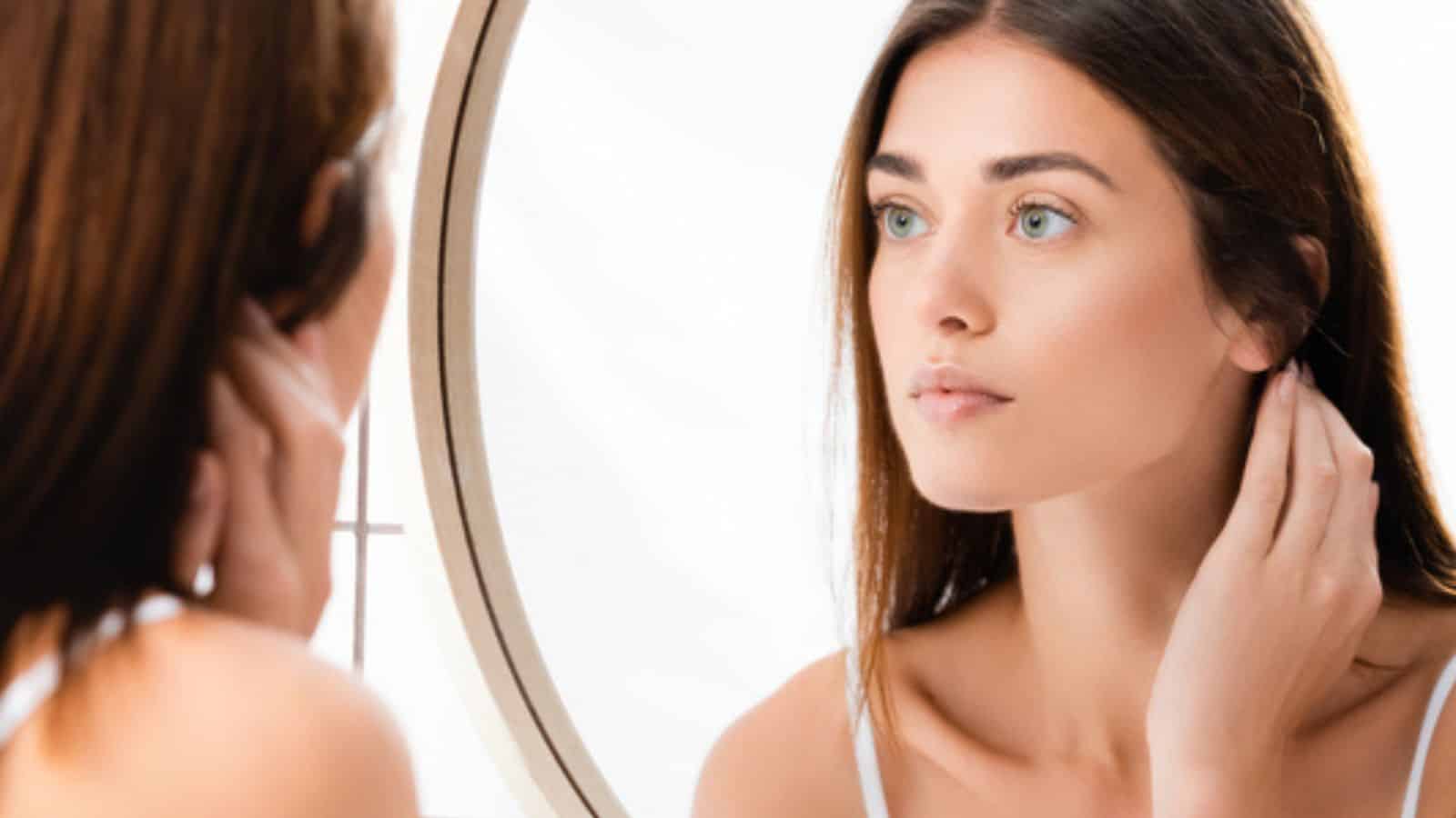 Young woman with perfect skin looking in mirror in bathroom