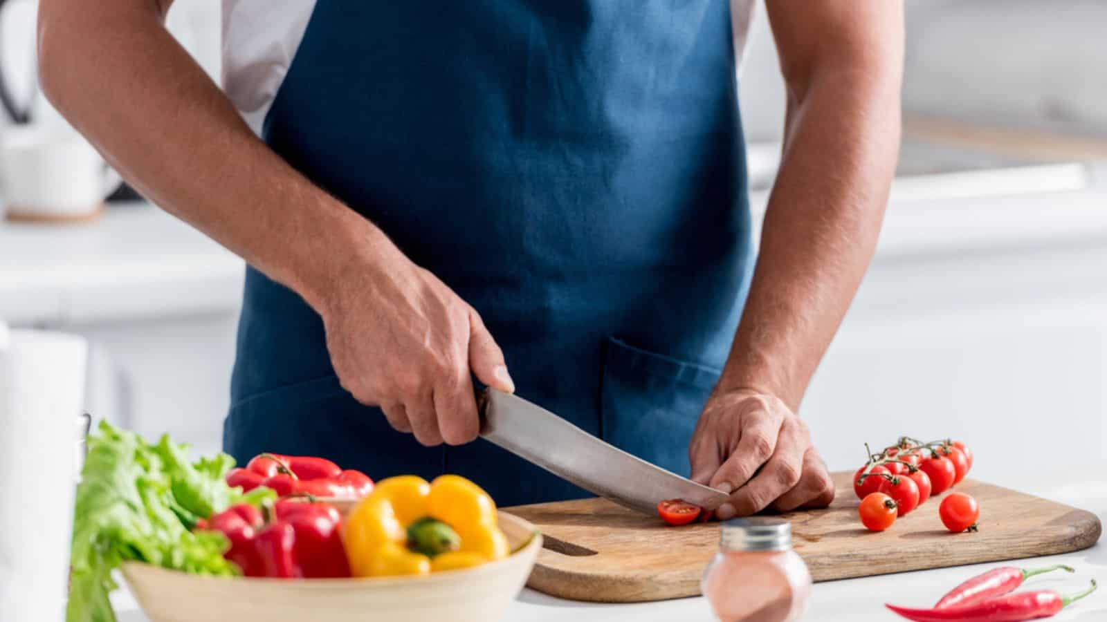 man cutting cherry tomatoes on chopping board