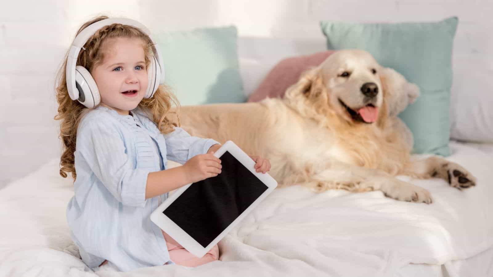 toddler baby on couch with earphones and tablet and dog