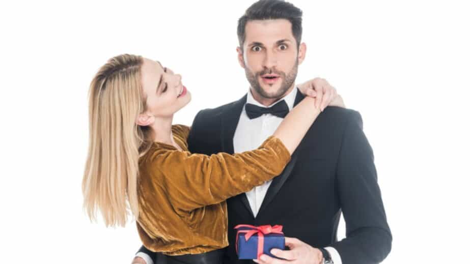 woman hugging shocked boyfriend in suit with wrapped gift